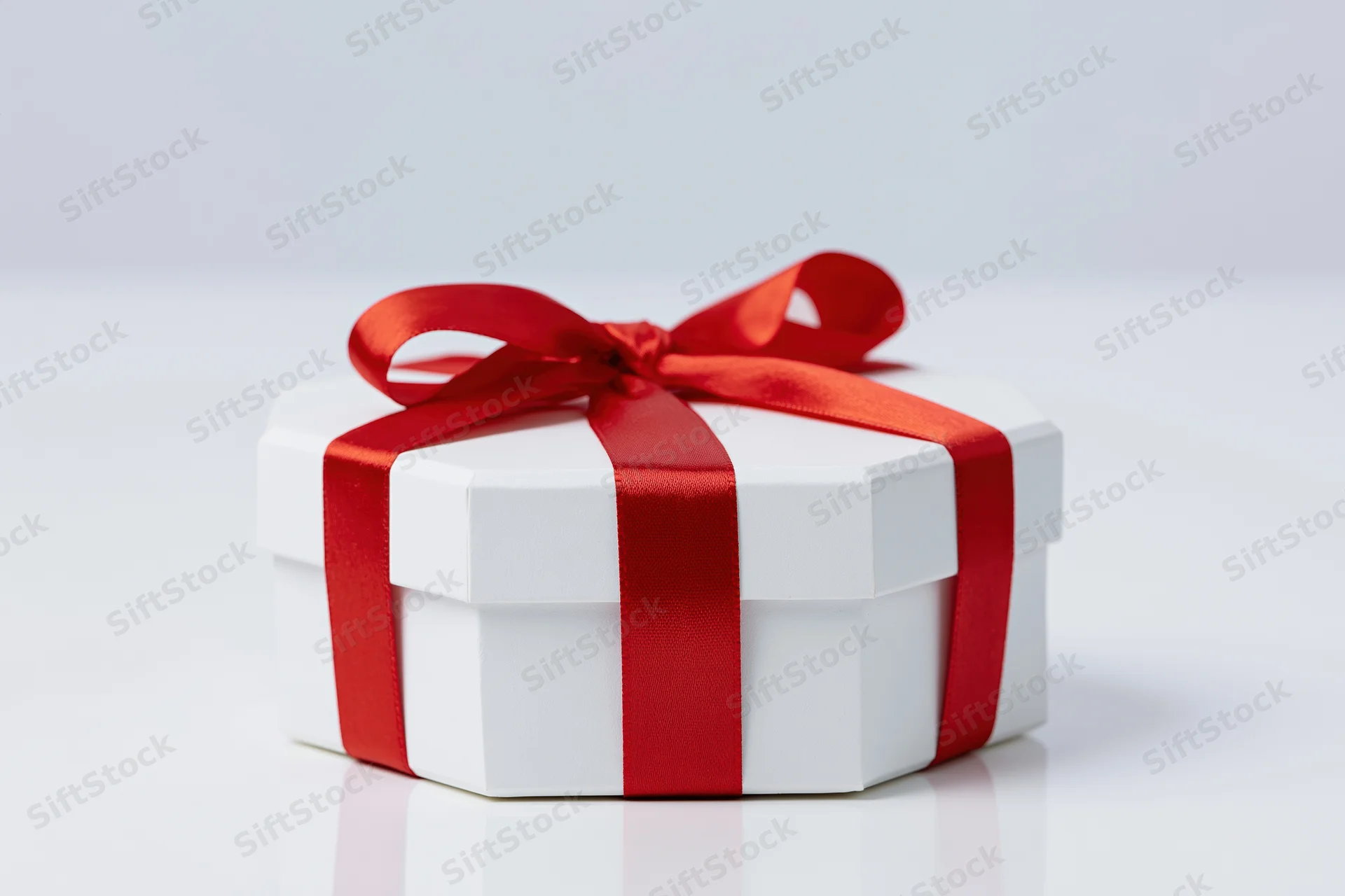 White octagonal gift box wrapped with red satin ribbon on white surface