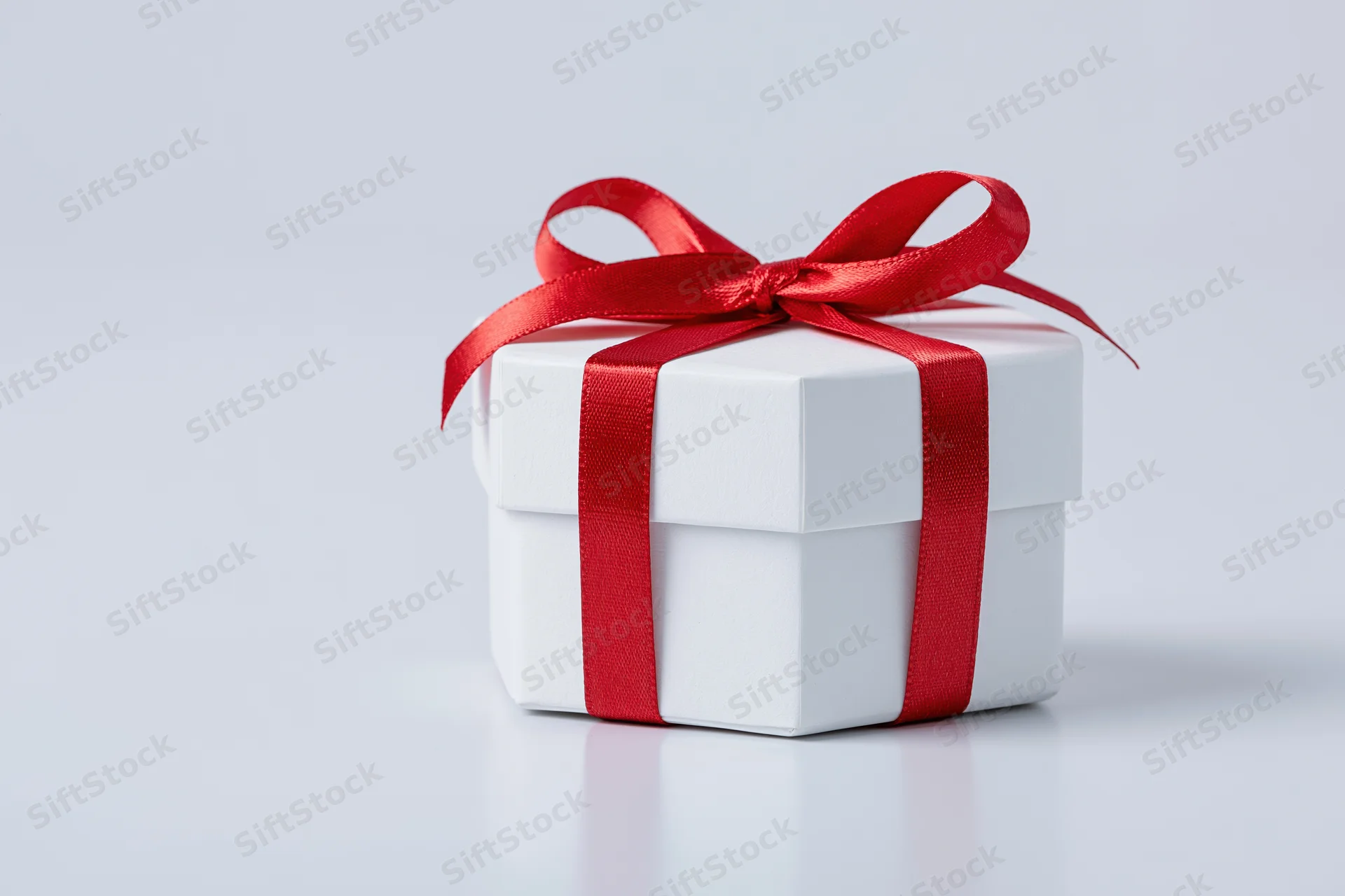 Small white octagonal gift box tied with red satin ribbon on white surface