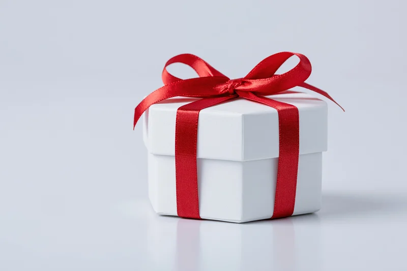 Small white octagonal gift box tied with red satin ribbon on white surface