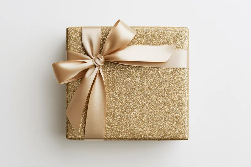 Square gift box wrapped in gold glitter paper with a satin ribbon bow on white background
