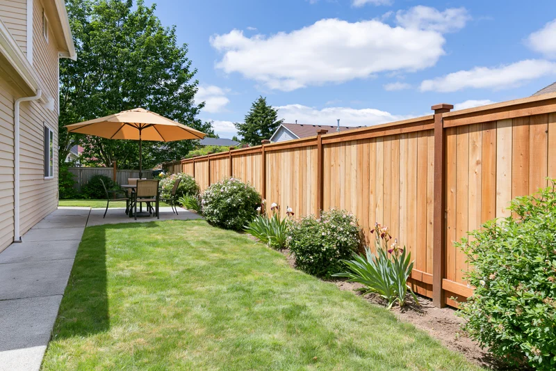 Suburban backyard with trimmed green lawn, wooden fence, and patio seating along a concrete pathway