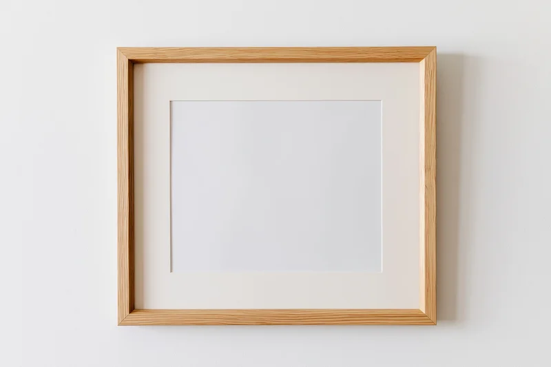 Light oak wooden picture frame with blank white interior hanging on a white wall