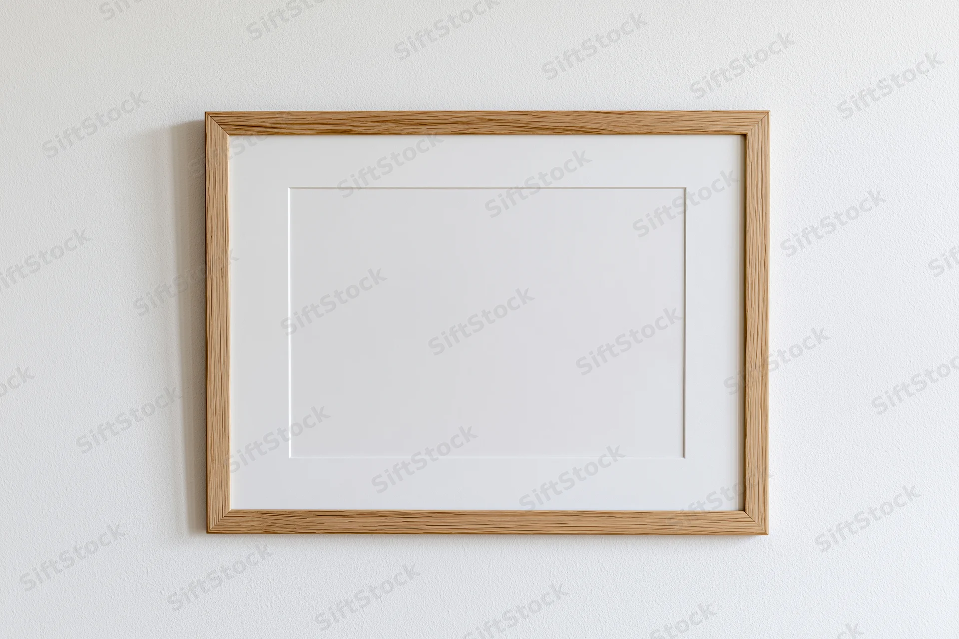 Light oak wooden picture frame with white mat board hanging on a white wall