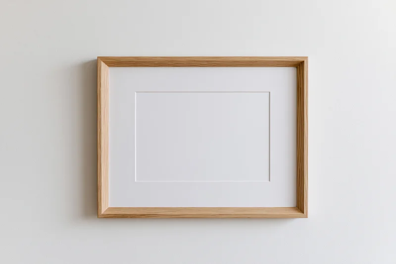Light oak wooden picture frame with white mat hanging on a plain white wall