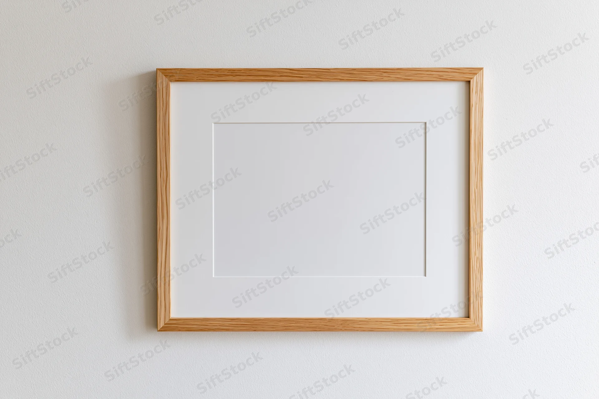Light oak wooden picture frame with white mat board hanging on a white wall