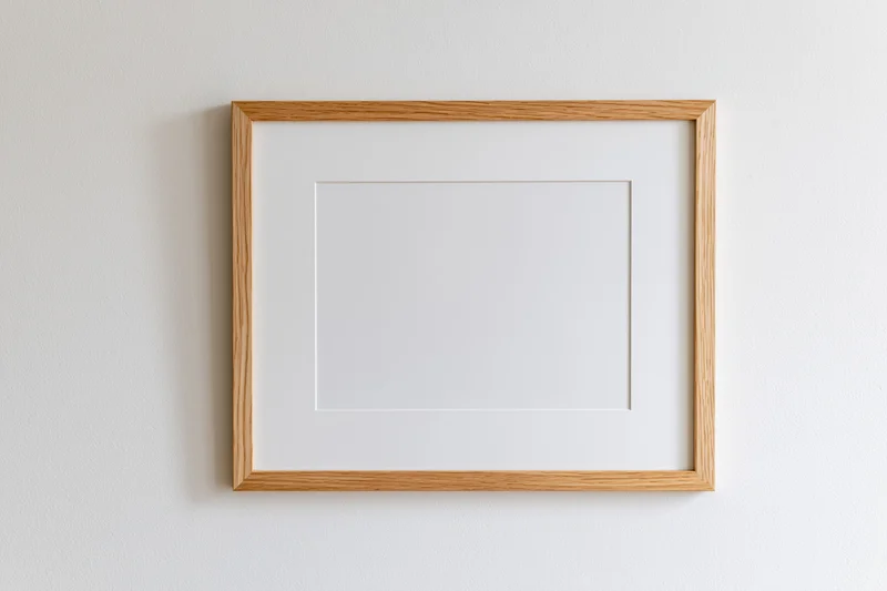Light oak wooden picture frame with white mat board hanging on a white wall
