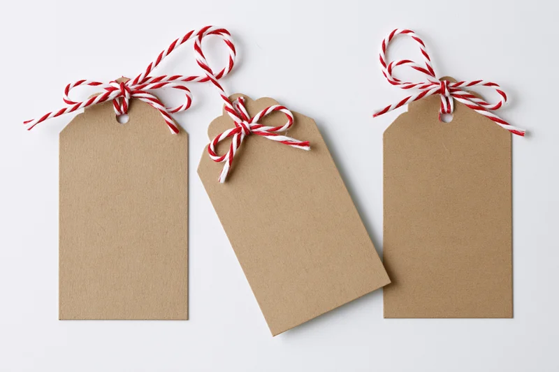 Three blank kraft paper gift tags tied with red and white string bows arranged side by side on white background