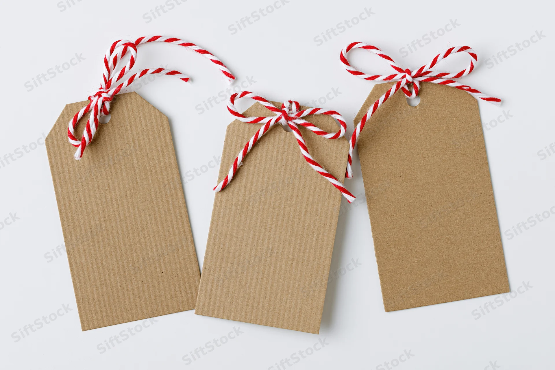 Three blank kraft paper gift tags with red and white striped string bows arranged side by side on white surface