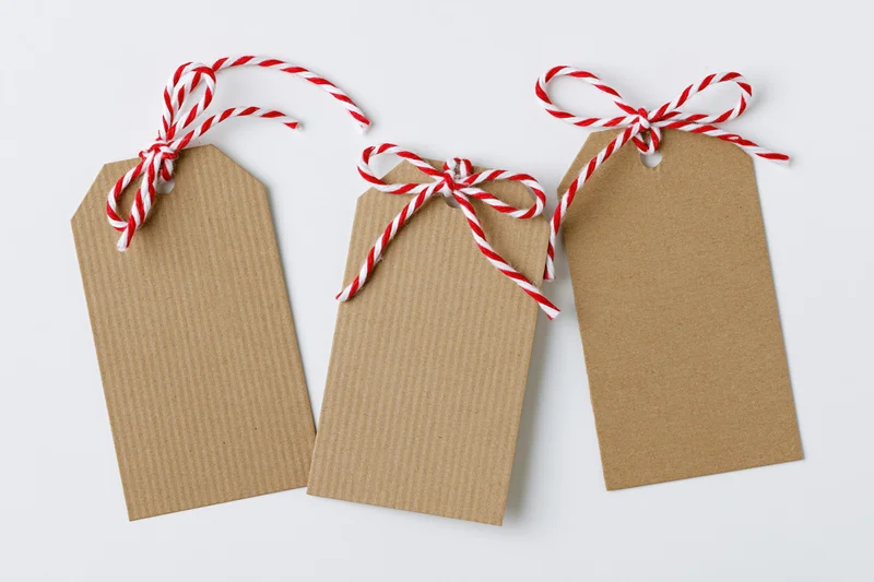Three blank kraft paper gift tags with red and white striped string bows arranged side by side on white surface
