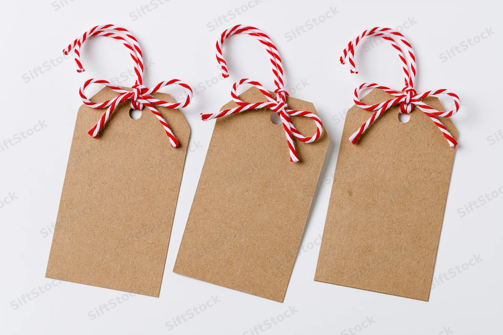 Three blank kraft paper gift tags with red and white striped string bows arranged side by side on white background