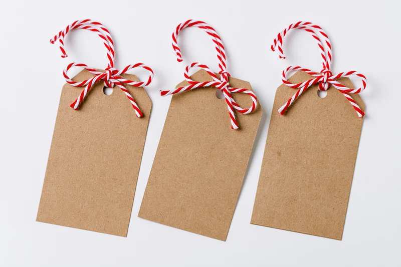 Three blank kraft paper gift tags with red and white striped string bows arranged side by side on white background