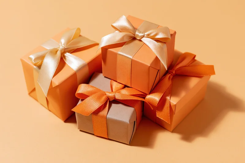 Four gift boxes wrapped in orange and beige paper with ribbons arranged in a cluster on an orange surface