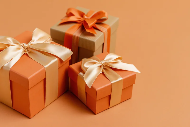 Three gift boxes wrapped with ribbons and bows arranged on an orange surface