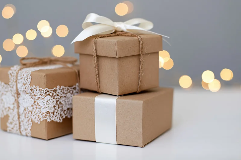 Three kraft paper gift boxes stacked and arranged on a white surface with bokeh lights in the background