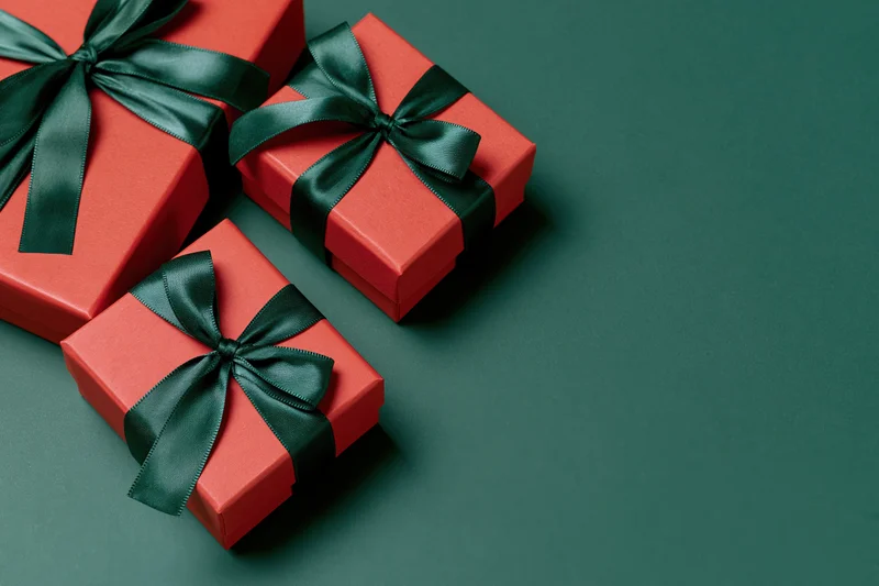 Three red gift boxes wrapped with dark green satin ribbon bows on a dark green surface