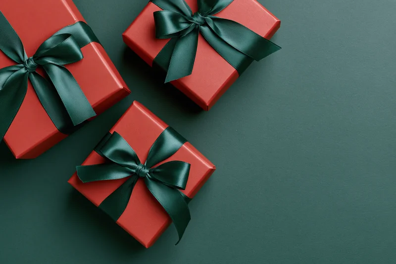 Three red gift boxes with dark green satin ribbon bows arranged on dark green surface