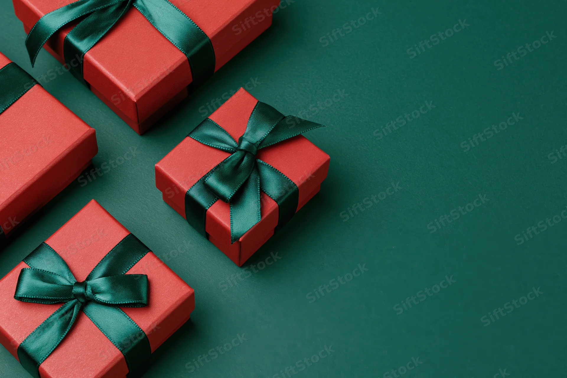 Red gift boxes wrapped with dark green satin ribbon bows on a green surface