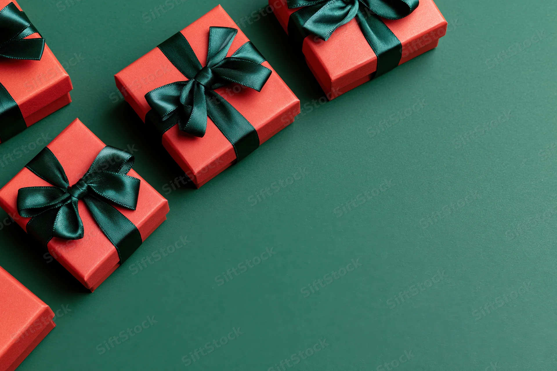 Red gift boxes wrapped with dark green satin ribbon bows arranged on green surface