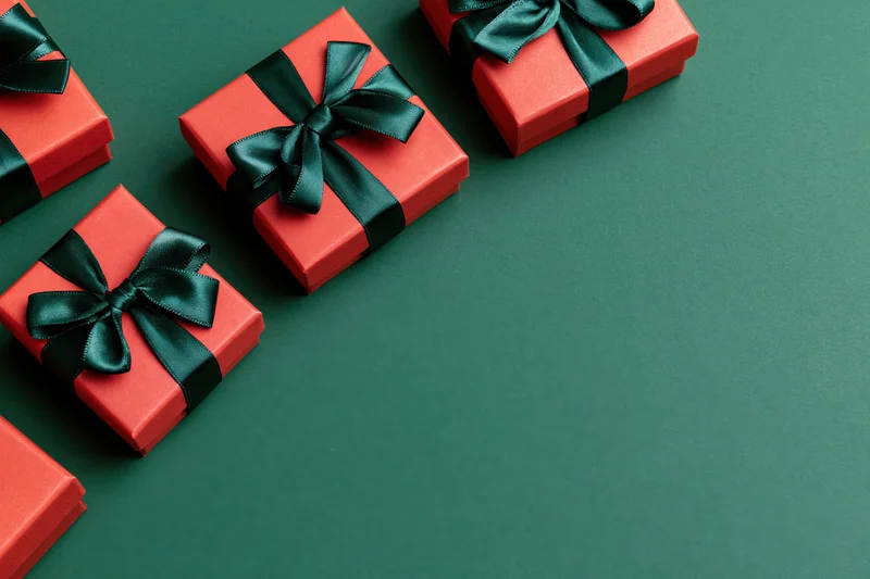 Red gift boxes wrapped with dark green satin ribbon bows arranged on green surface