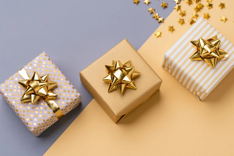 Three gift boxes with gold foil bows arranged diagonally on a two-tone background