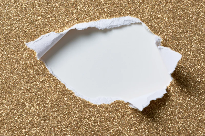Torn hole in gold glitter paper revealing white space