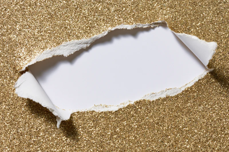 Torn hole in gold glitter paper revealing white space