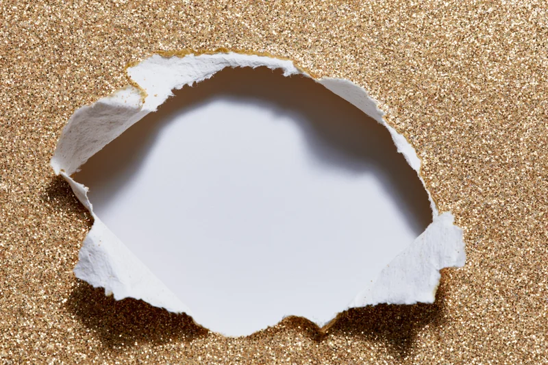 Torn hole in gold glitter paper revealing white space