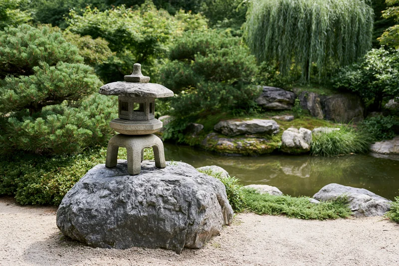 Stone lantern on a rock in a traditional japanese garden with pond and greenery