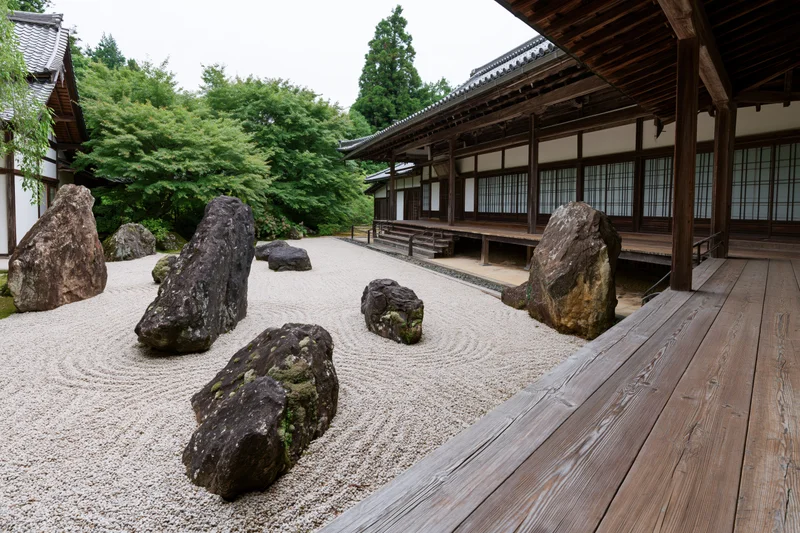 Traditional japanese zen garden with raked gravel and large rocks arranged in a courtyard beside a wooden temple building