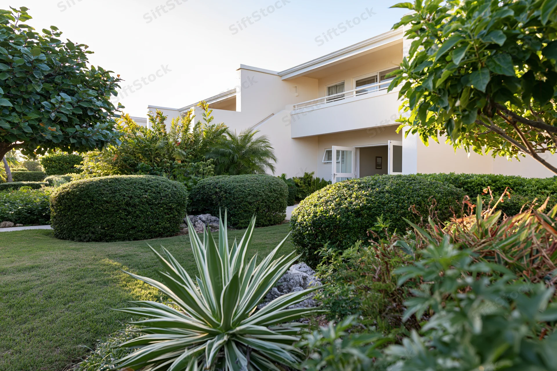 Tropical resort garden courtyard with manicured lawn and lush greenery surrounding a white building with balcony and open door
