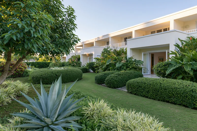 Tropical resort garden courtyard with manicured lawn and lush greenery surrounding a white building with balconies and entrance
