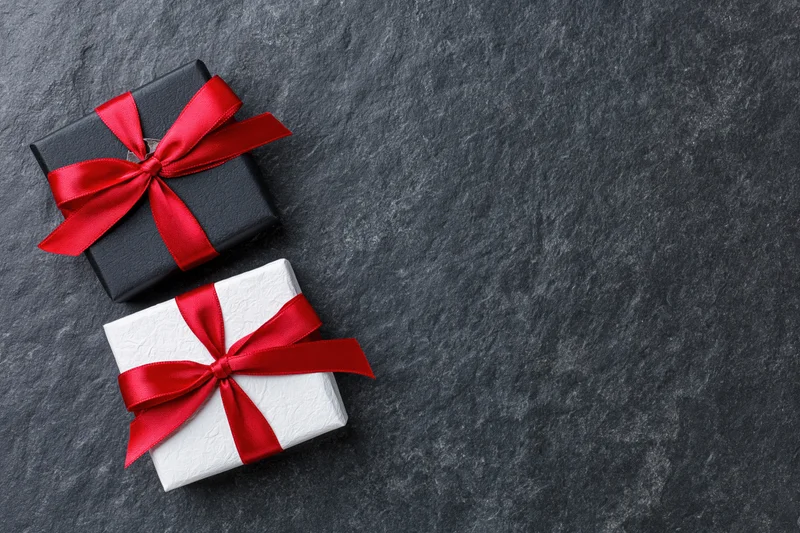 Two gift boxes wrapped in black and white paper with red ribbons on dark stone surface