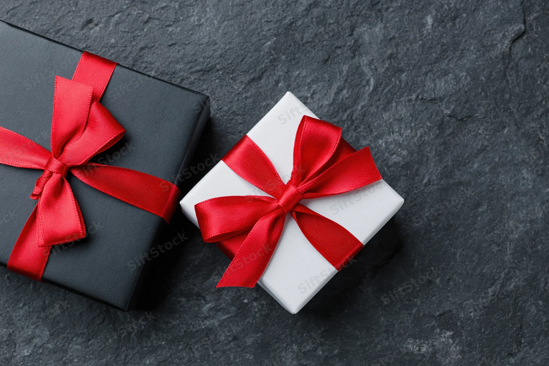 Two gift boxes wrapped in black and white paper with red ribbons on dark stone surface