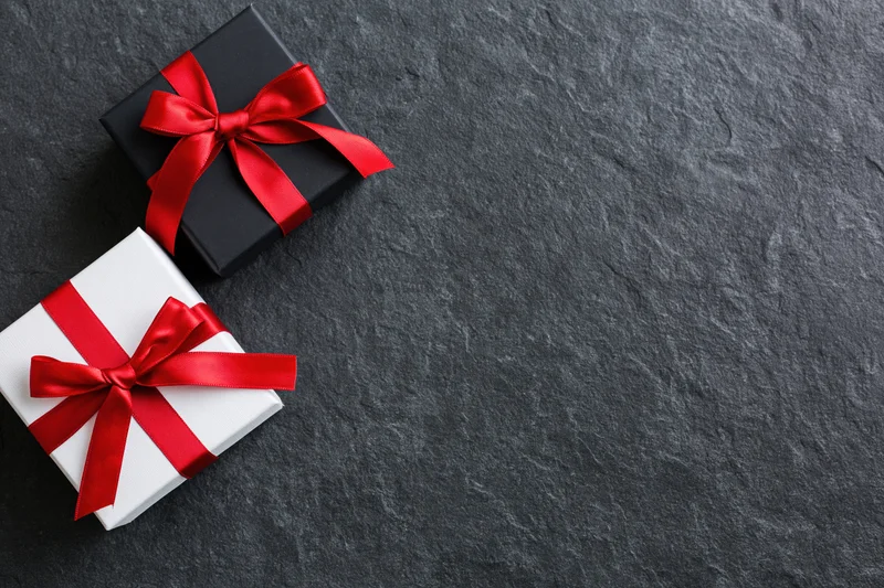 Two gift boxes wrapped in black and white paper with red ribbons on a dark stone surface