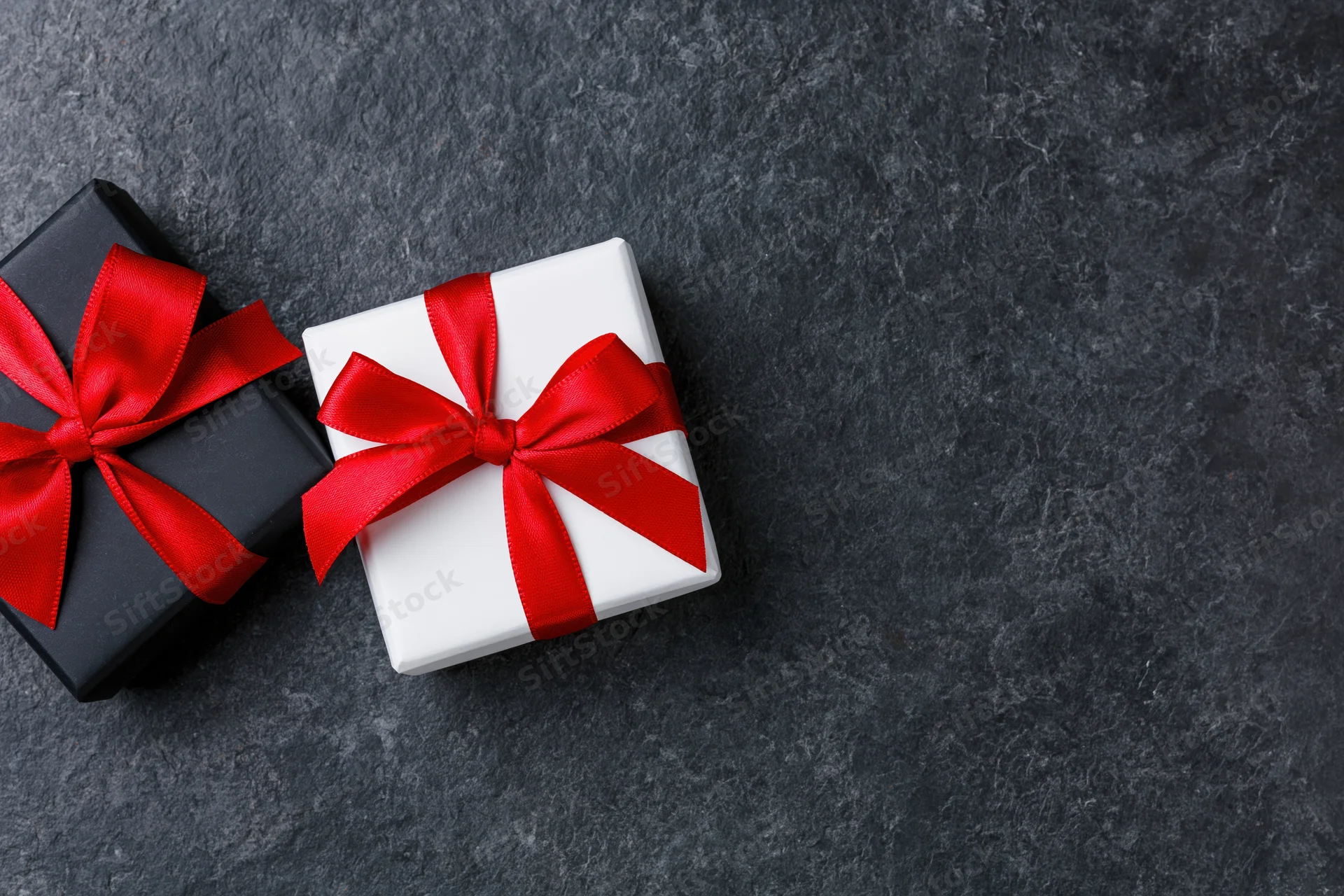 Two gift boxes wrapped in black and white paper with red ribbons on dark stone surface