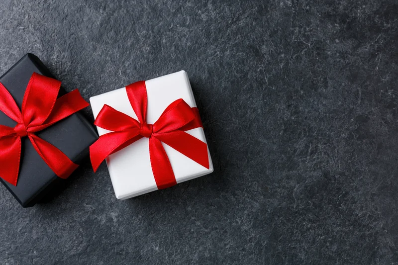 Two gift boxes wrapped in black and white paper with red ribbons on dark stone surface