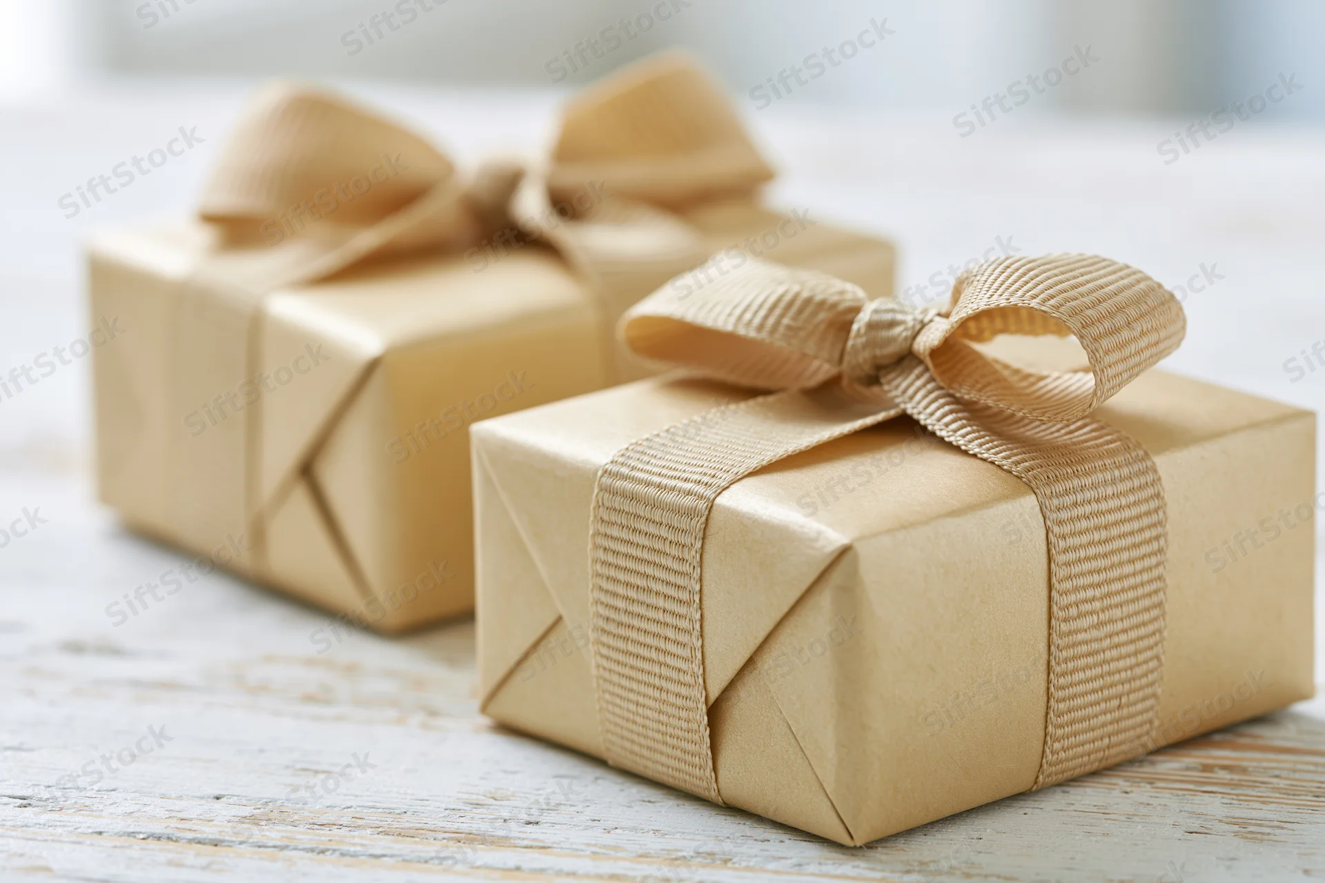 Two gift boxes wrapped in matte gold paper with ribbons on a wooden table