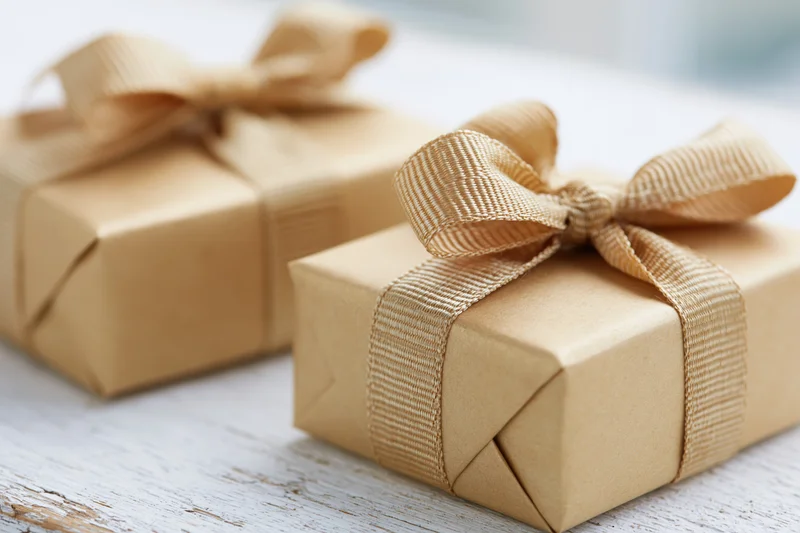 Two gift boxes wrapped in matte gold kraft paper with ribbons on a white wooden surface