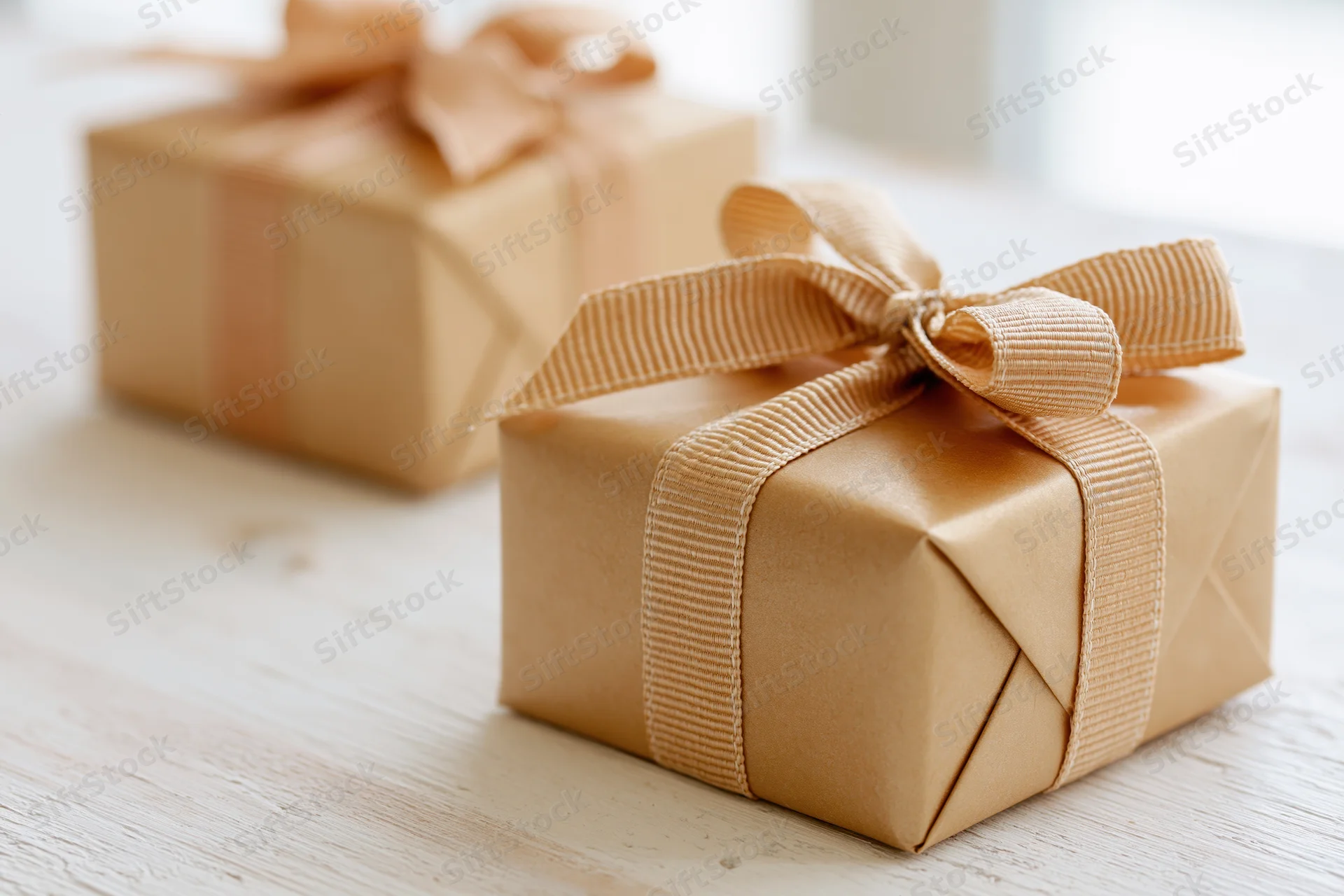 Two gift boxes wrapped in matte gold kraft paper with ribbons on a wooden table