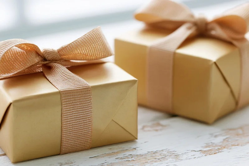 Two gold-wrapped gift boxes with peach ribbons on a rustic white wooden table