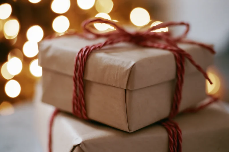 Two kraft paper gift boxes wrapped with red twine bows stacked in front of warm bokeh lights
