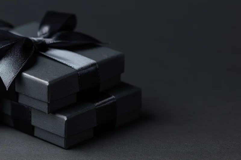Two matte black gift boxes stacked and tied with satin ribbon on dark surface
