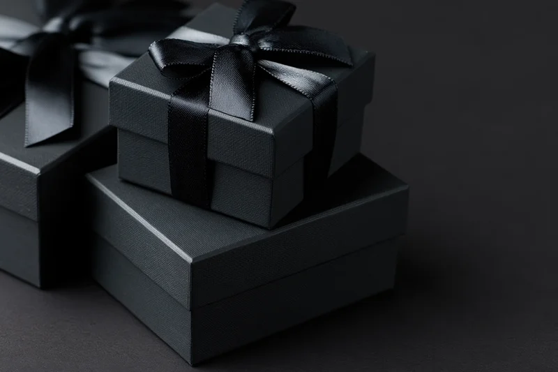 Stacked matte black gift boxes tied with ribbons on dark surface
