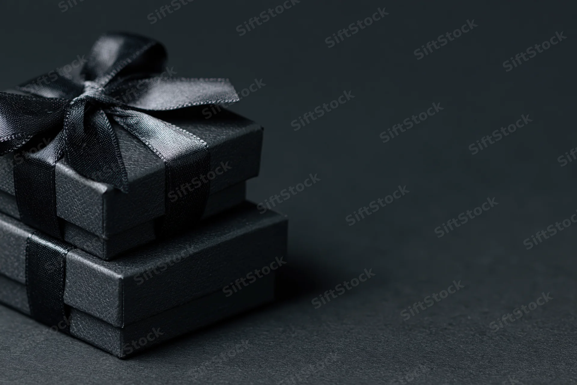 Two matte black gift boxes stacked and tied with ribbon on dark surface
