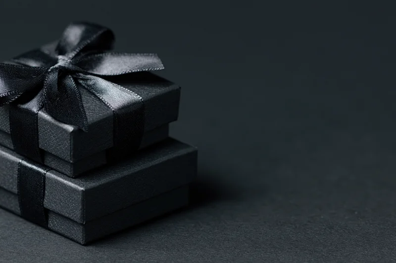 Two matte black gift boxes stacked and tied with ribbon on dark surface