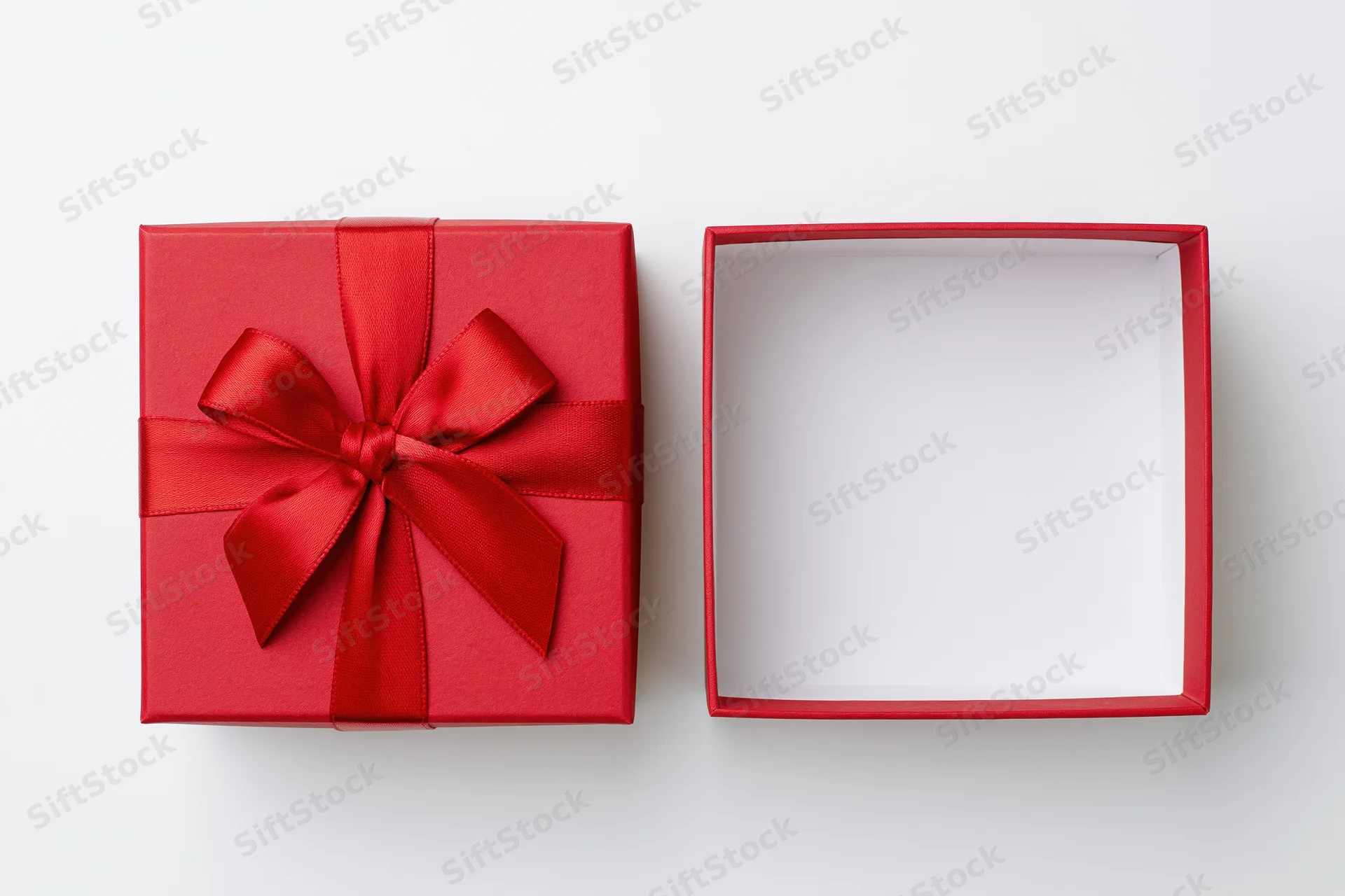 Two red gift boxes one closed with ribbon bow and one open on white surface