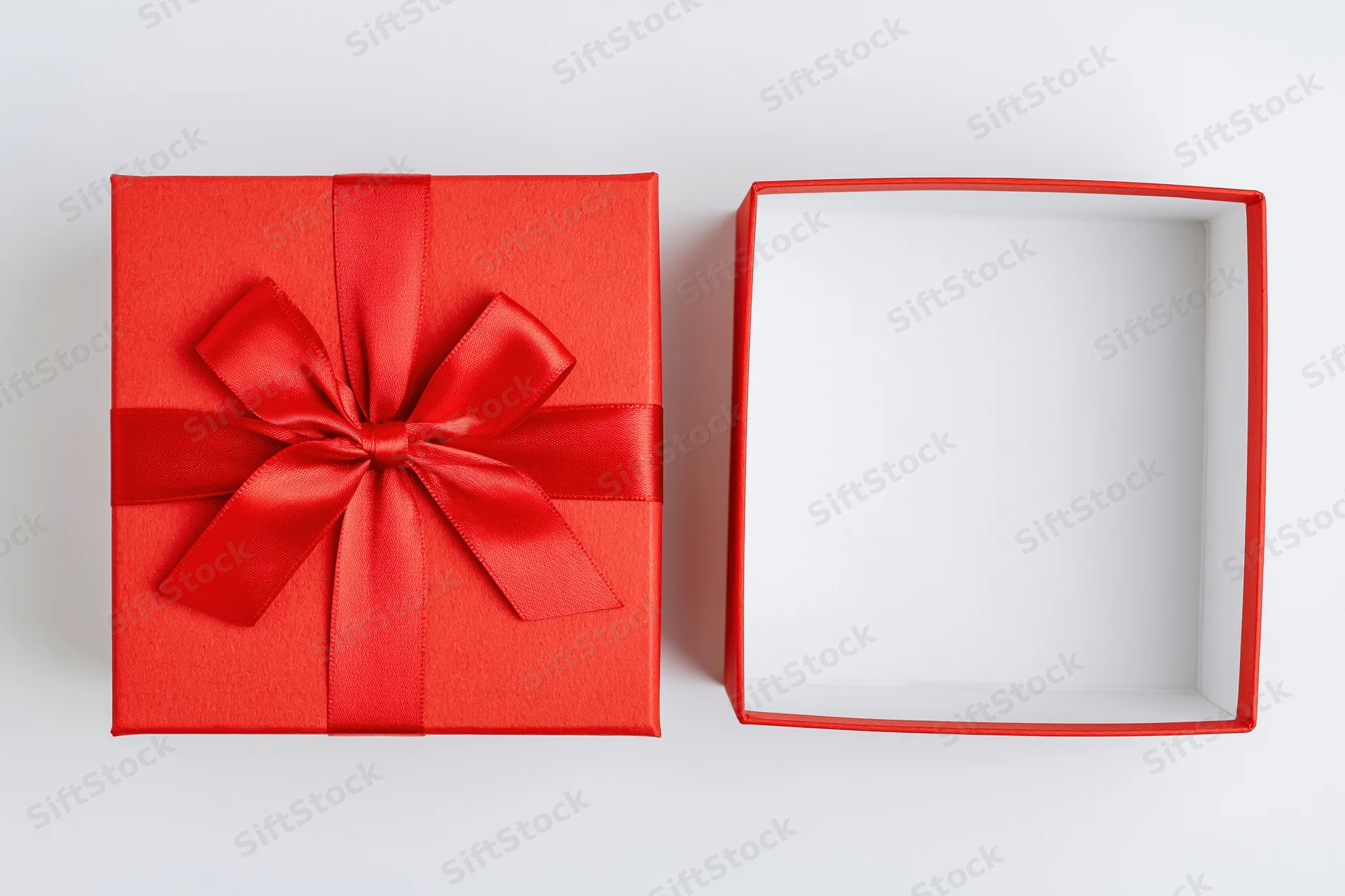 Red gift box with ribbon bow beside open empty box on white surface