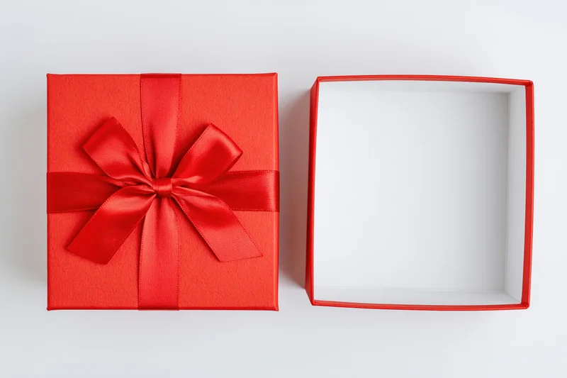 Red gift box with ribbon bow beside open empty box on white surface
