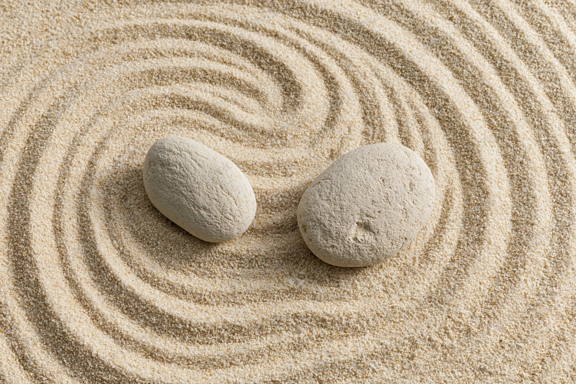 Two smooth stones resting on raked sand in a zen garden pattern
