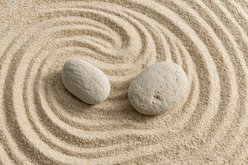 Two smooth stones resting on raked sand in a zen garden pattern